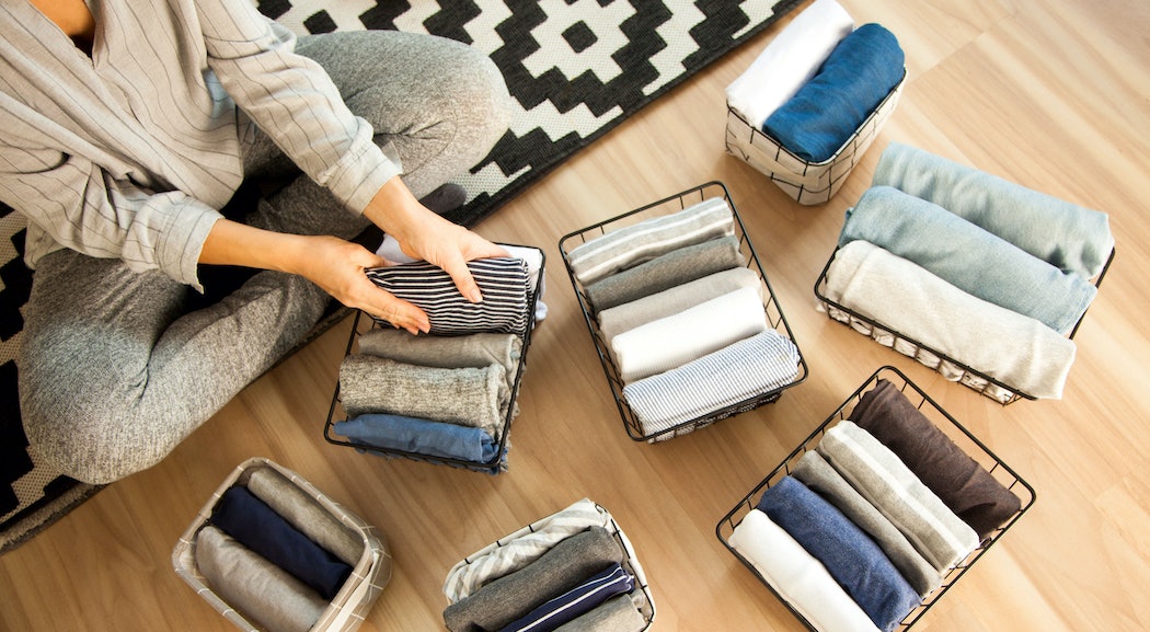 Frau sitzt auf dem Boden und sortiert Kleidungsstücke