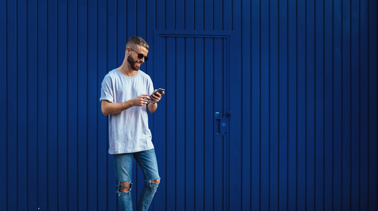 Junger Mann mit Smartphone in der Hand vor blauem Container