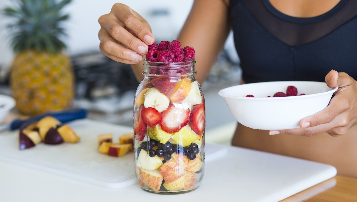 Frau in Sportkleidung füllt Schraubglas mit frischem Obst