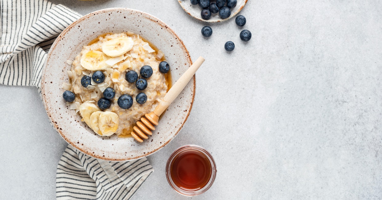 Schüssel gefüllt mit Porridge, Blaubeeren, Banane und Honig