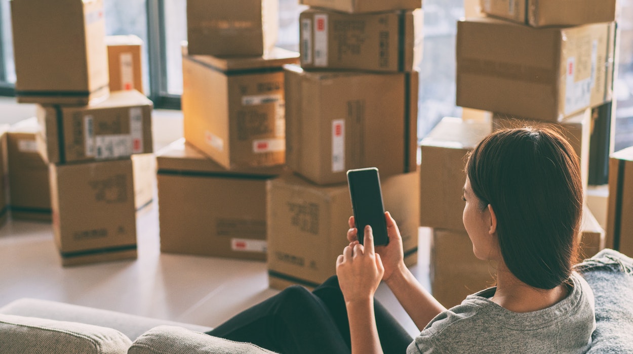 Junge Frau mit Smartphone vor Umzugskartons