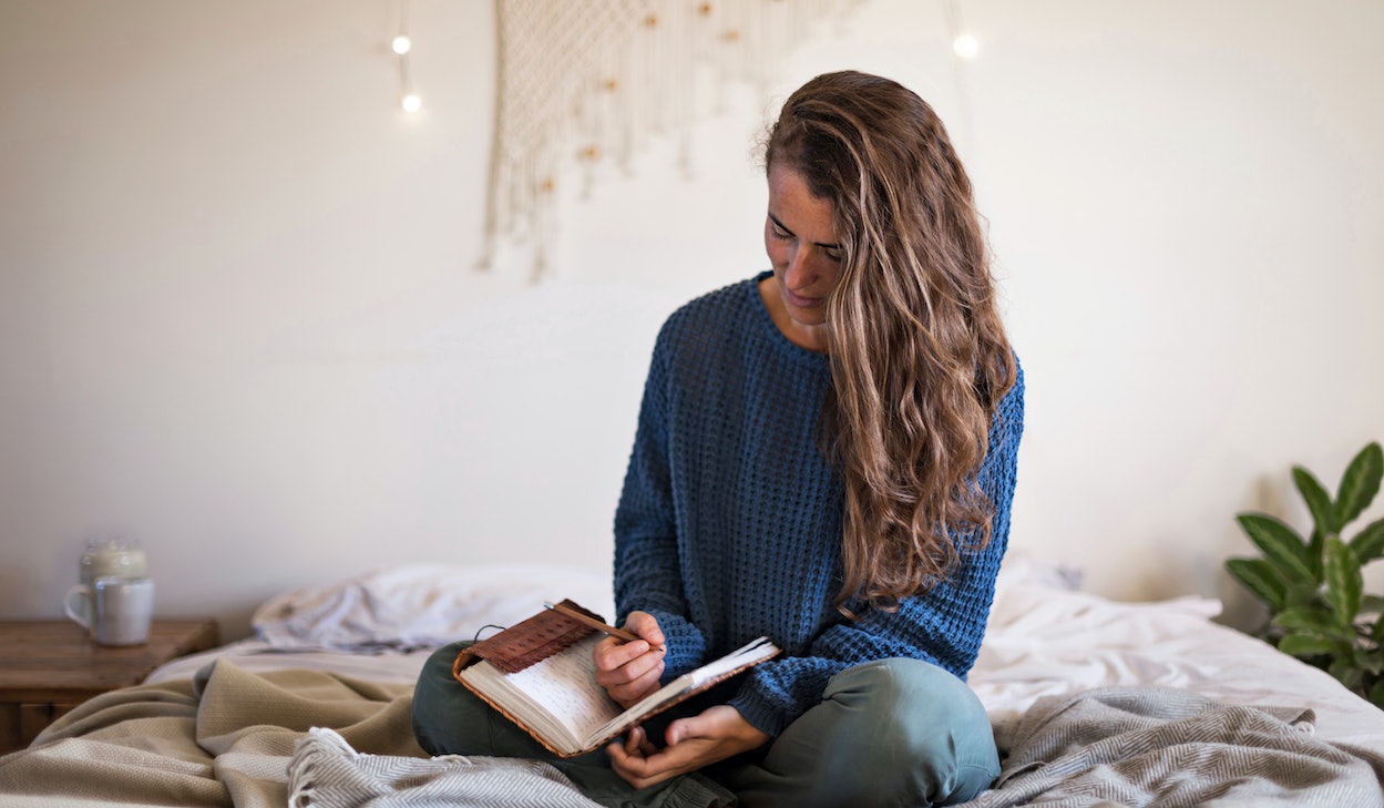 Junge Frau sitzt auf Bett und schreibt in Tagebuch