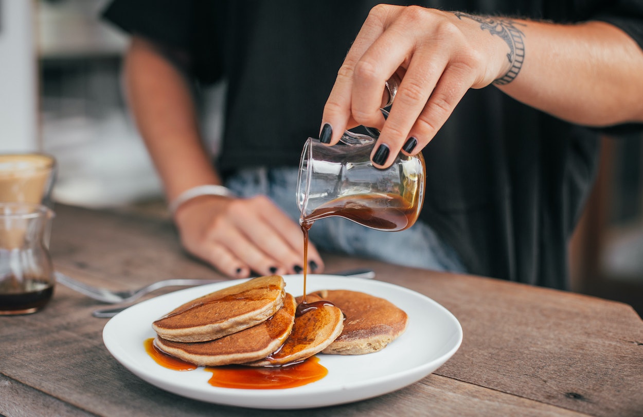 Frau gießt Ahornsirup über Pancakes