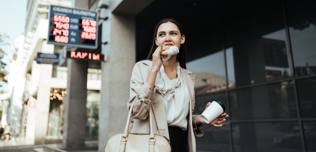 Frau hält Kaffeebecher und isst Snack unterwegs