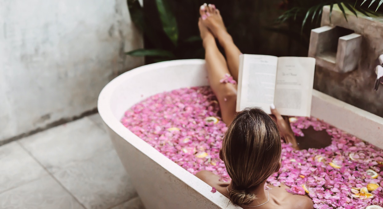 Frau nimmt Bad in Wanne mit rosa Blüten